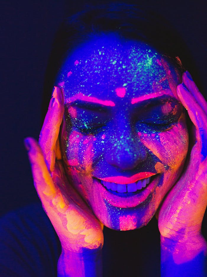 A woman with vivid neon face paint under ultraviolet light at a festival.