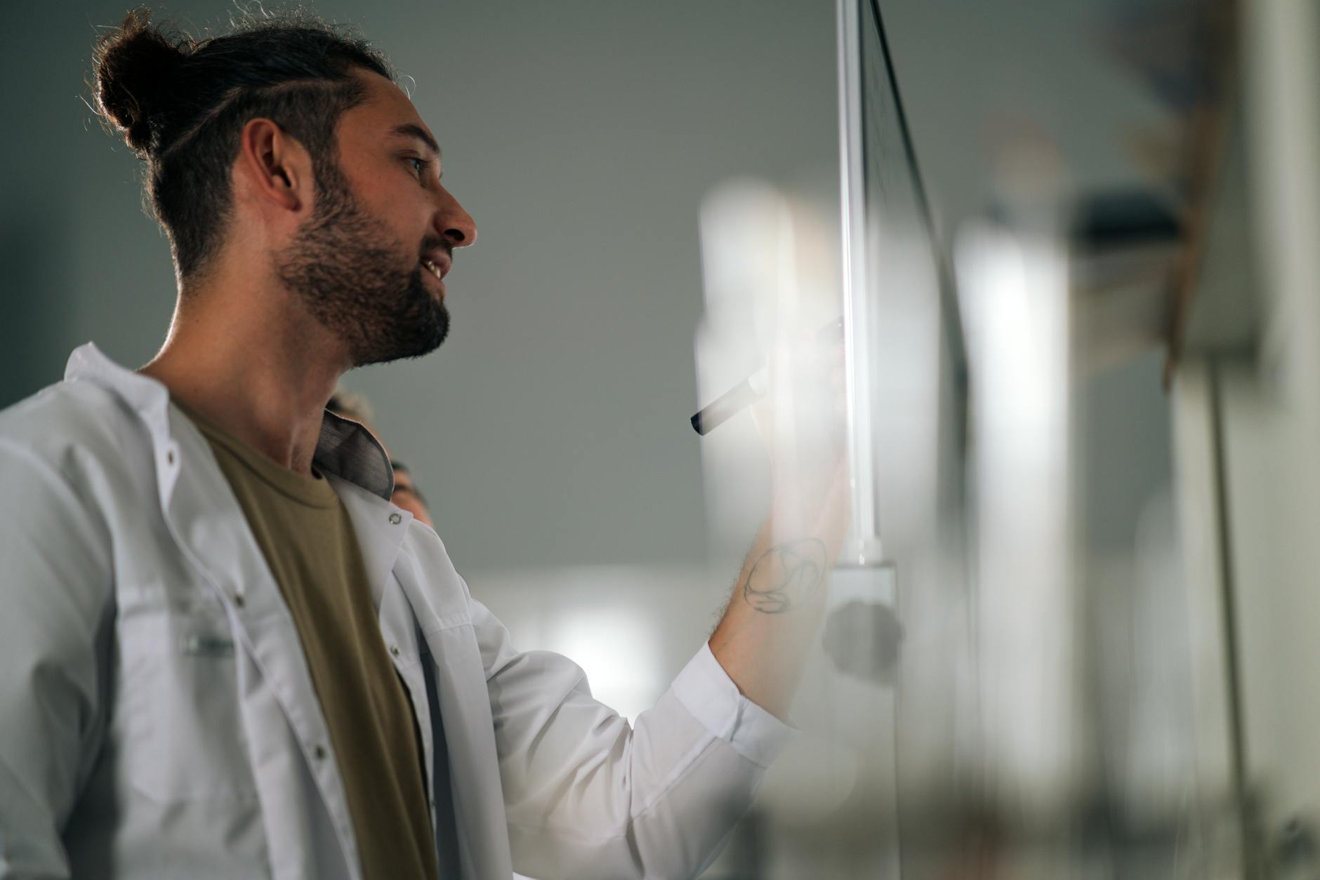 A young scientist writing on a whiteboard in a lab setting, focused on research ideas.