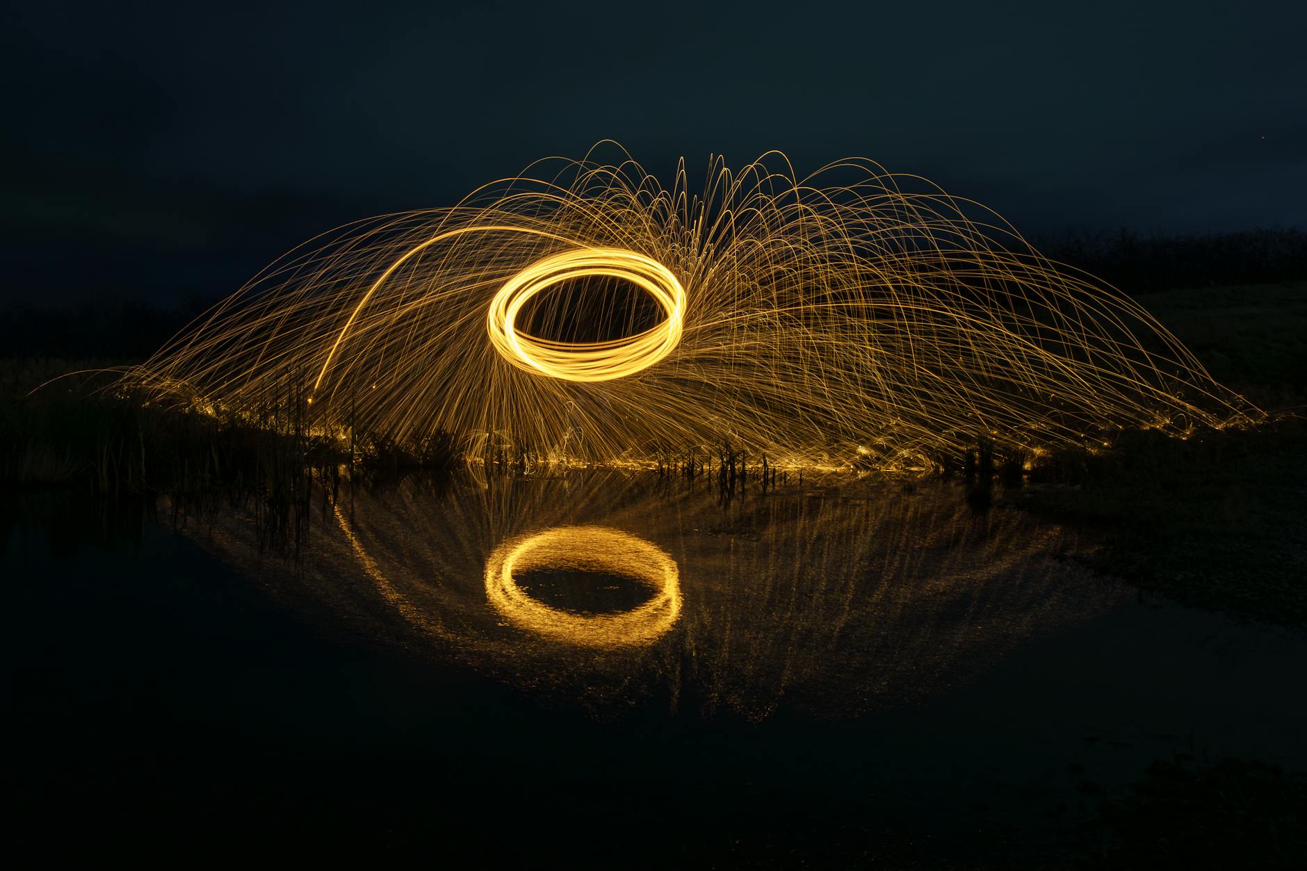 Captivating long exposure of wire wool spinning over water creating brilliant light patterns.