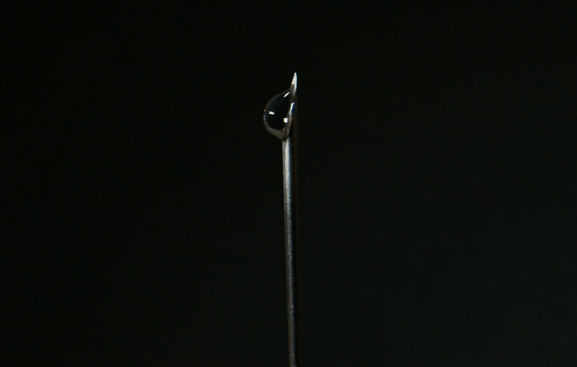 Close-up of a steel needle with a water droplet against a dark background.