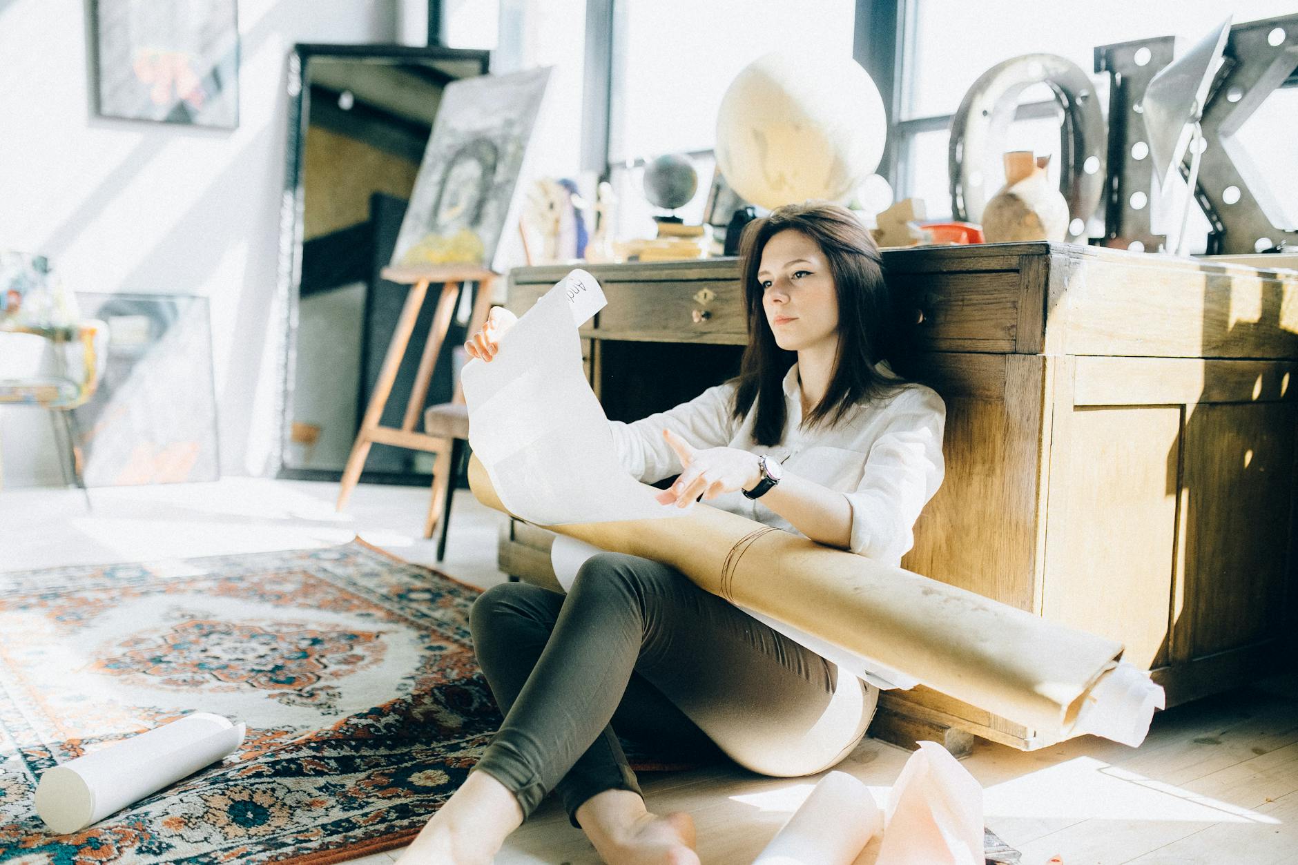Female architect in a sunlit studio, examining architectural plans with artistic decor.