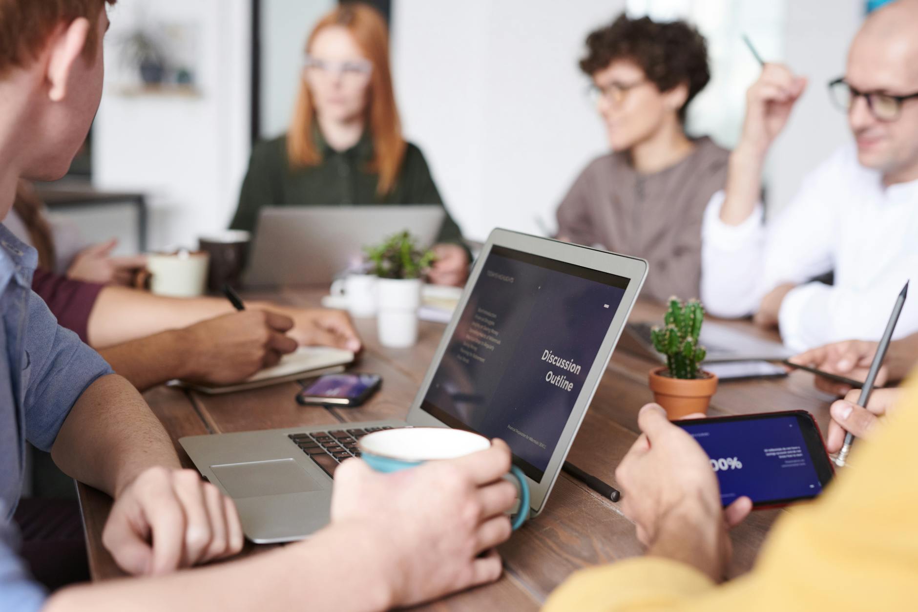 A diverse group of professionals collaborating with laptops and tablets in a modern office setting.
