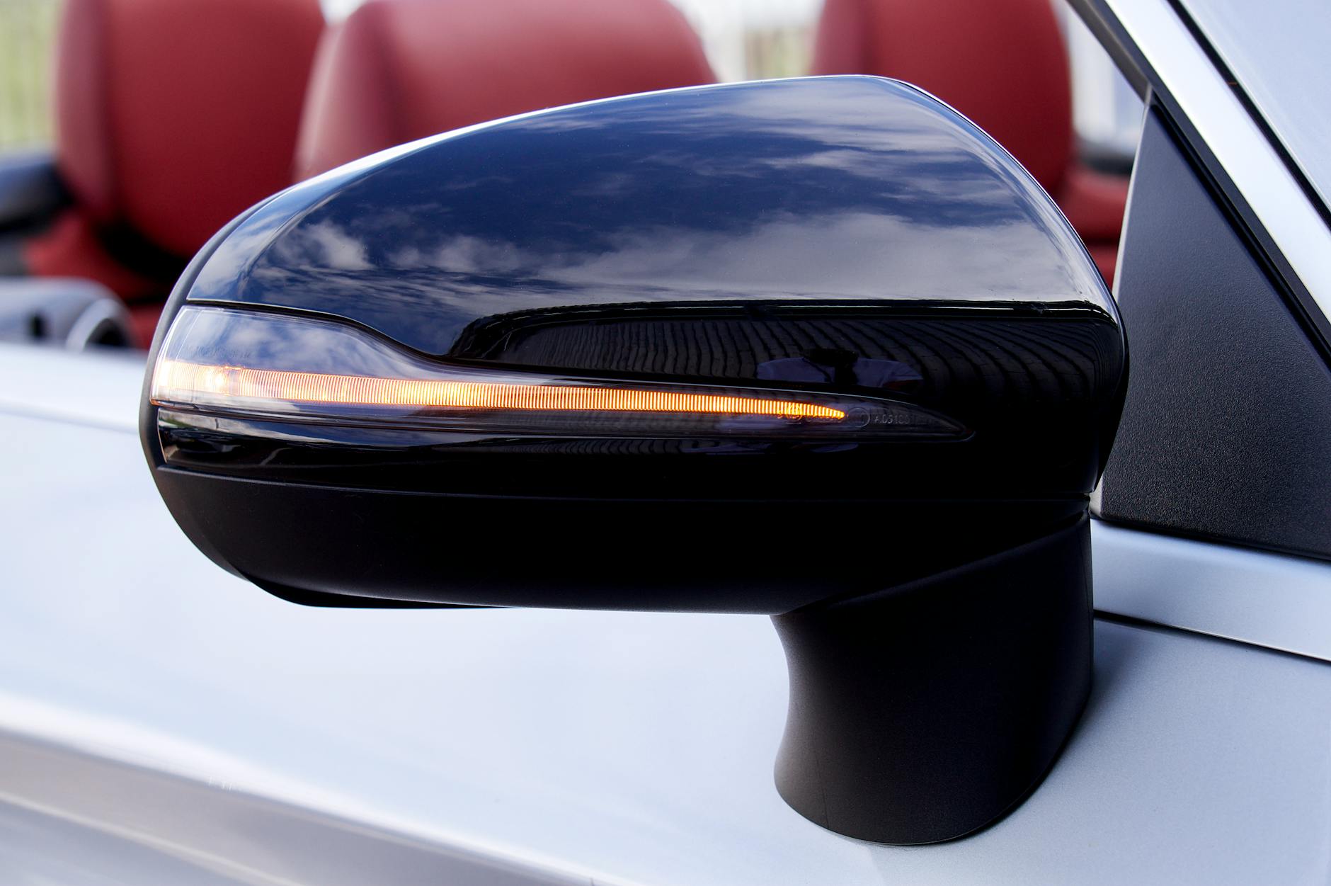 Close-up image of a sleek car side mirror reflecting the sky, highlighting modern automotive design.